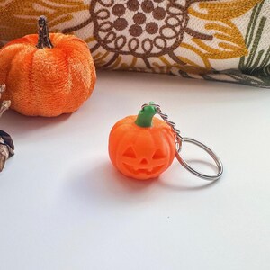 Pumpkin keychain with keyring on white background beside fall decorations – Halloween keyring charm.