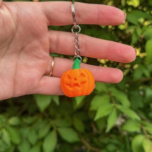 Hand holding a smiling pumpkin jack o’ lantern keychain – cute Halloween accessory.