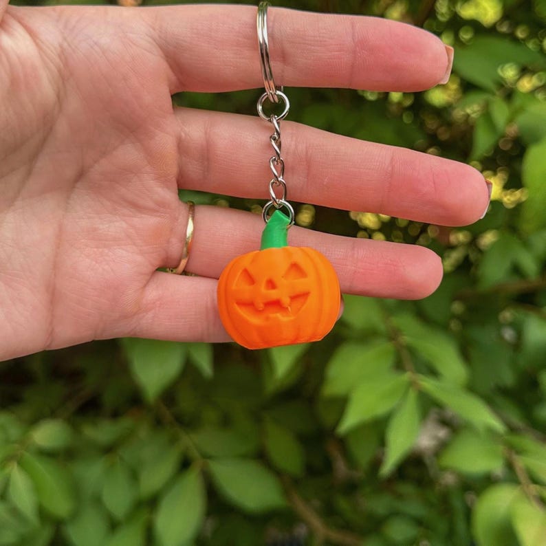 Hand holding a smiling pumpkin jack o’ lantern keychain – cute Halloween accessory.