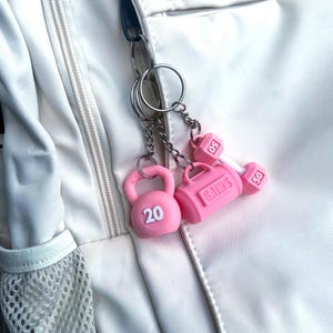 Pink fit life keychain set attached to silver keychains hooted to a white backpack.