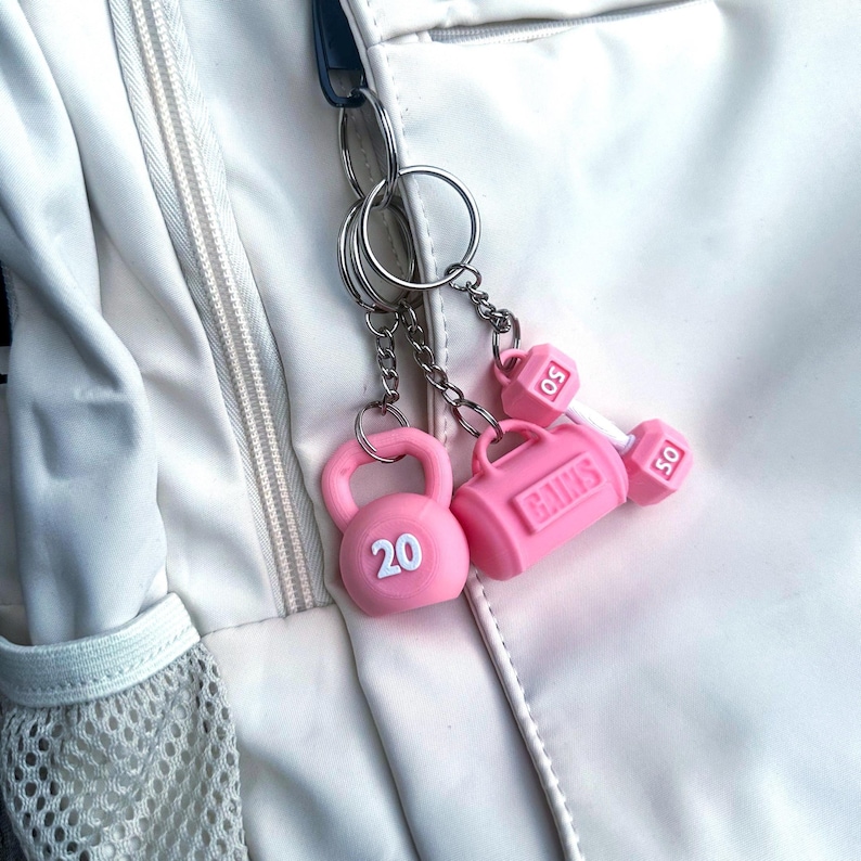 Pink fit life keychain set attached to silver keychains hooted to a white backpack.