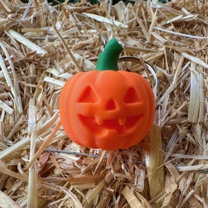 Close-up of jack o’ lantern pumpkin keychain on hay – carved Halloween pumpkin design.