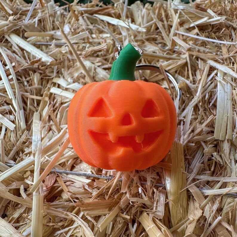 Close-up of jack o’ lantern pumpkin keychain on hay – carved Halloween pumpkin design.