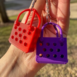 Two small, colorful, plastic bags with handles. The bag on the left is red and the bag on the right is purple. Both bags have a grid pattern with holes throughout the surface.