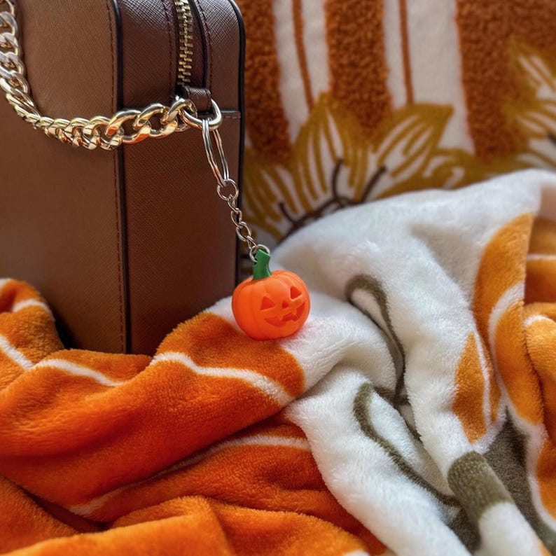 Pumpkin keychain hanging on a purse chain with fall blanket background – spooky season accessory.