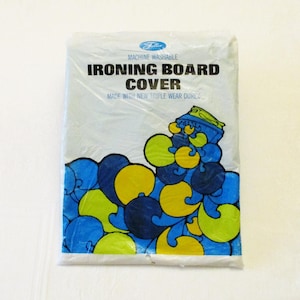 Pode incluir: Uma capa de t&aacute;bua de engomar embalada com o texto "Ironing Board Cover" em letras pretas em negrito. A capa tem um design abstrato azul, amarelo e verde. A embalagem diz "Machine Washable" e "Made with New Triple Wear Durex."