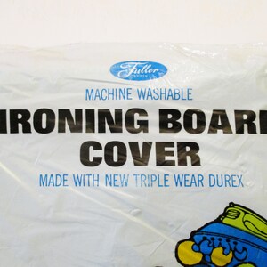 Pode incluir: Capa de t&aacute;bua de engomar branca em embalagem de pl&aacute;stico. A capa tem o texto "MACHINE WASHABLE IRONING BOARD COVER" em preto e azul. O logotipo da Fuller Brush Co. est&aacute; no topo.