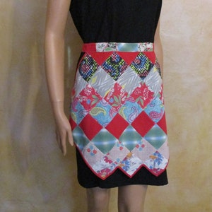 May include: A patchwork apron with a red waistband and a scalloped hem. The apron features a diamond pattern with various fabric designs, including floral, paisley, and geometric prints. The colors include red, blue, green, gray, and white.