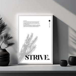 Puede incluir: Un póster en blanco y negro con una mano que se estira hacia arriba y la palabra "STRIVE" impresa en letras negras en negrita. El póster está enmarcado en un marco blanco y está colgado en una pared blanca.