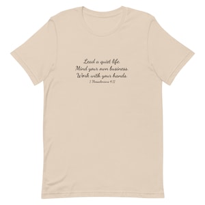 Puede incluir: Una camiseta beige con texto negro que dice "Lead a quiet life. Mind your own business. Work with your hands. 1 Thessalonians 4:11"