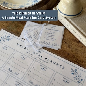 Pode incluir: Uma folha de planeamento semanal de refeições com detalhes florais azuis e um conjunto de pequenos cartões unidos por um anel intitulados The Dinner Rhythm, A Simple Meal Planning Card System, listando opções como Rotisserie Chicken Meals.