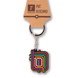 May include: A colorful PVC keychain featuring a stylized design of a transit system map. The keychain is attached to a silver key ring and comes with a brown paper tag that reads "PVC Keychain" and "Transit Tees".