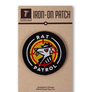 May include: Iron-on patch featuring a cartoon rat wearing a hat and a trench coat, with a red target and the words "RAT PATROL" around it.