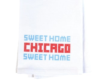 May include: White kitchen towel with blue and red cross-stitched text that reads "Sweet Home Chicago Sweet Home".