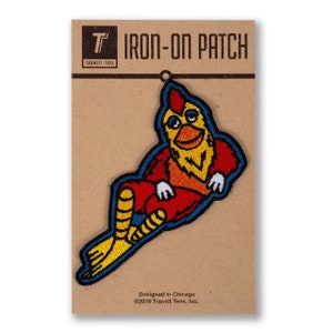May include: Iron-on patch featuring a cartoon chicken wearing a red and blue outfit, sitting with its legs crossed. The patch is on a brown card with the text "IRON-ON PATCH" and "Transit Tees" in white. The text "Designed in Chicago ©2016 Transit Tees, Inc." is also on the card.