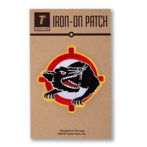 May include: Iron-on patch featuring a black cartoon animal with red eyes and sharp teeth inside a red and yellow target. The patch is on a brown card with the text "T IRON-ON PATCH TRANSIT TEES Designed in Chicago ©2016 Transit Tees, Inc."