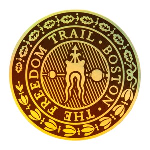 May include: A gold and brown circular sticker with the text "The Freedom Trail Boston" and "Trail" in a larger font. The sticker features a stylized image of a tree with a single leaf and a small arrow pointing upwards.