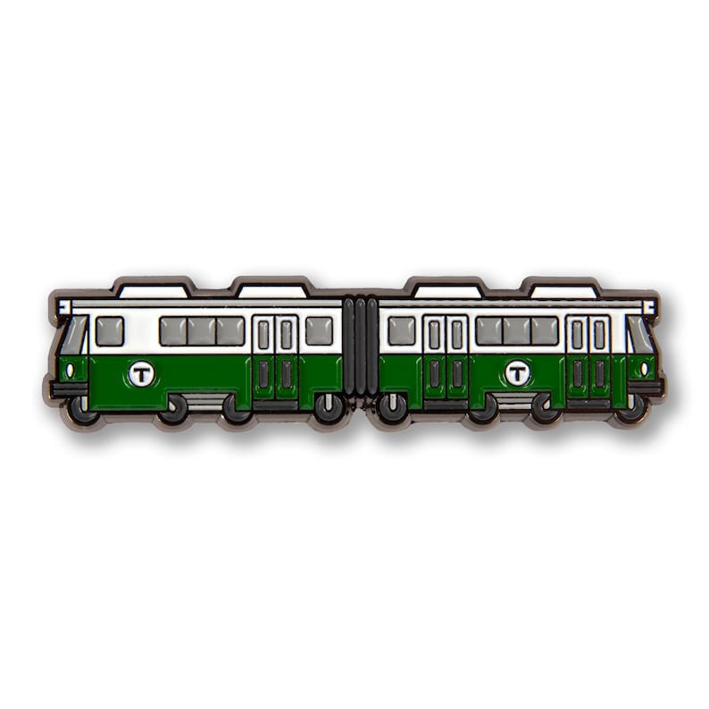 May include: A green and white train badge featuring the letter "T". The design depicts a detailed train carriage with windows and doors. This pin is likely a souvenir or collectible item, with a detailed design.