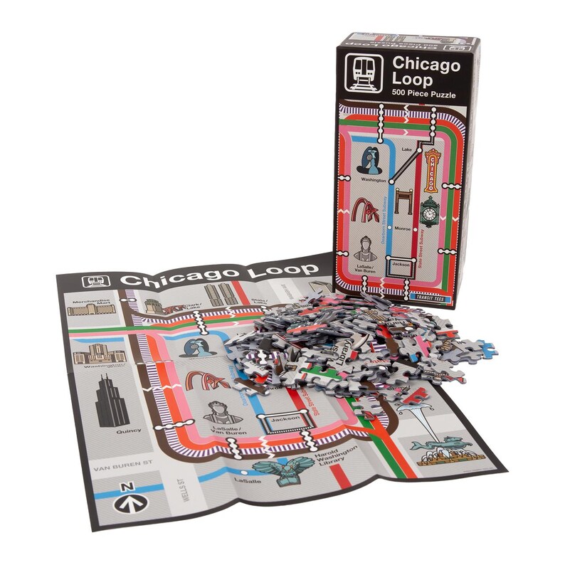 Op de afbeelding: Een 500-delige puzzel van de Chicago Loop 'L' treinkaart. De puzzel ligt uitgespreid op een tafel, met de doos ernaast. De doos is rood, wit en zwart met een afbeelding van de 'L' treinkaart erop. De tekst op de doos luidt "Chicago Loop 500 Piece Puzzle".