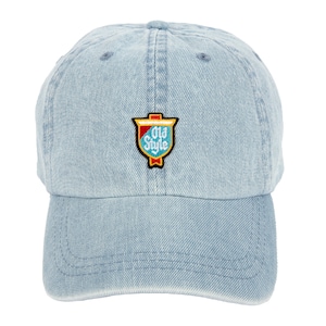 May include: A light blue denim baseball cap with an embroidered patch featuring a red, yellow, and blue shield with the text "Old Style" in white.