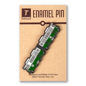 May include: Enamel pin depicting a green and white train carriage. The pin is displayed on a brown card with the text "ENAMEL PIN" and the Transit Tees logo. The card also includes the text "Designed and Made in Chicago" and copyright details.