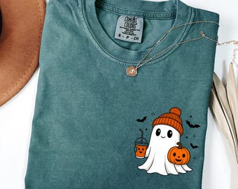 May include: Blue spruce-colored t-shirt with a Halloween-themed graphic. The graphic features a cartoon ghost wearing an orange beanie, holding a pumpkin spice drink and a jack-o'-lantern. The shirt has a crew neck and short sleeves.