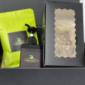 Peut inclure: Un coffret noir contenant un sac vert, un flacon pompe noir et une boîte noire avec une fenêtre. Le sac vert et le flacon pompe portent le texte "Heka Herbal" et un logo. La boîte noire a une fenêtre montrant le contenu.