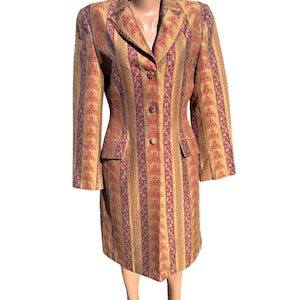 May include: A vintage, knee-length dress suit with a striped pattern in gold, burgundy, and purple. The suit features a collared blazer with three buttons, two front pockets, and long sleeves. The dress suit is displayed on a mannequin.