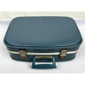 May include: A rectangular blue suitcase with rounded corners, featuring a matching blue handle, a silver-toned metal trim along the center, and two metallic latches on the front for secure closure of the hard-shell travel case.