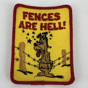 May include: A rectangular embroidered patch with a yellow background and a red border. It features a cartoon dog tangled in barbed wire between two fence posts, with the text FENCES ARE HELL! in red letters and black stars above.