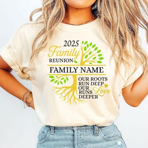May include: A cream-coloured t-shirt featuring a family reunion design. The design includes a tree graphic with the text "2025 Family Reunion" and "Family Name." Additional text reads "Our Roots Run Deep, Our Runs Deeper Love."