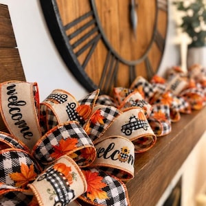 K&ouml;nnte beinhalten: Eine dekorative Bandgirlande mit einem sich wiederholenden Muster aus schwarz-wei&szlig; karierten Lastwagen, orangefarbenen K&uuml;rbissen und Herbstbl&auml;ttern auf beigem Grund, wobei Abschnitte des Bandes mit dem Wort welcome in schwarzer Schrift bedruckt sind.