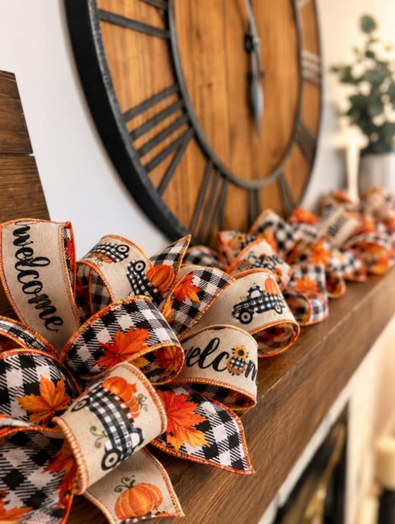K&ouml;nnte beinhalten: Eine dekorative Bandgirlande mit einem sich wiederholenden Muster aus schwarz-wei&szlig; karierten Lastwagen, orangefarbenen K&uuml;rbissen und Herbstbl&auml;ttern auf beigem Grund, wobei Abschnitte des Bandes mit dem Wort welcome in schwarzer Schrift bedruckt sind.