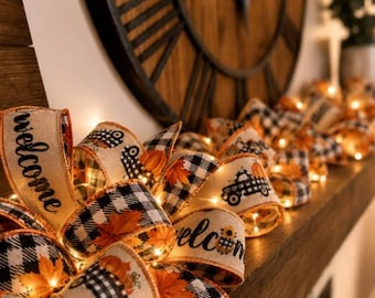 May include: A decorative ribbon garland featuring a beige burlap texture with a black and white buffalo check pattern, orange autumn leaves, pumpkins, and black truck graphics. The ribbon includes the word welcome and integrated warm fairy lights.