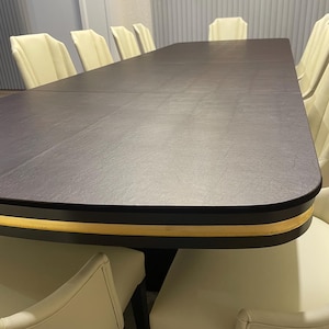 May include: A long, dark brown dining table with a gold trim around the edge. The table is surrounded by off-white chairs with a curved back.