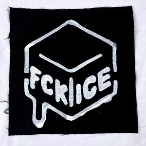 Puede incluir: Parche de tela negra cuadrada con un diseño geométrico blanco y la palabra "FCRICE" en una fuente goteante. El parche tiene un borde sin rematar.