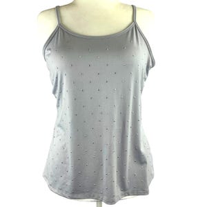 May include: A light gray camisole top with thin spaghetti straps. The top is adorned with numerous small, silver-colored embellishments scattered across the fabric. The garment is displayed on a mannequin.
