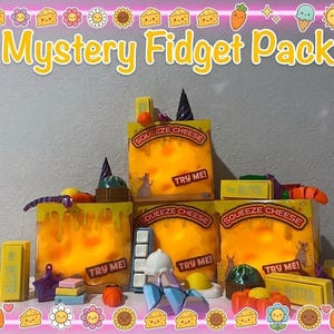 May include: A Mystery Fidget Pack featuring three yellow boxes labeled Squeeze Cheese with Try Me text. The display includes various small colorful fidget toys like butter sticks, a purple worm, a white ice cube tray, and a fried egg.