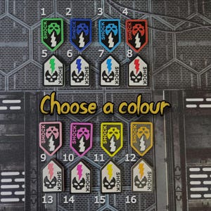 May include: A collection of sixteen colorful game tokens with the word "SHOCK" and a skull graphic. Each token is a different color, including green, blue, red, pink, and yellow. The text "Choose a colour" is also visible.