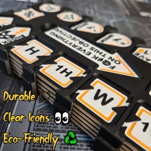 May include: Black organizer with white and orange icons, including arrows, numbers, and the text "F@ck Everything On This Objective." The organizer has the words "Durable," "Clear Icons," and "Eco-Friendly" in the image.