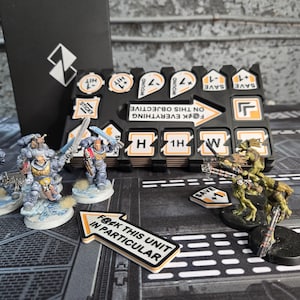 May include: A tabletop gaming scene featuring miniature figures and game tokens. The figures are painted in various colors and posed in action. Tokens include phrases like "F@ck this unit in particular" and "F@ck everything on this objective".