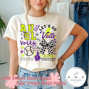 Könnte beinhalten: Cremefarbenes T-Shirt mit einem Grafikdesign. Das Design zeigt den Text "AU SL Volts" in Neongrün und Lila, einen Baseball, eine karierte Schleife und den Text "Athletes Unlimited Softball League".