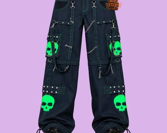 May include: Black cargo pants featuring neon green skull graphics on the pockets and lower legs. The pants include multiple straps, silver-toned metal chains, studded detailing, and mesh accents. The text Bold Stitch Studio is visible on the upper right.