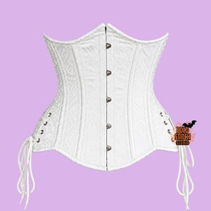 May include: A white corset featuring a subtle geometric diamond pattern, a front busk closure with silver-toned metal clasps, and side lacing with white cords. The garment displays the text Bold Stitch Studio with a small black bat graphic.