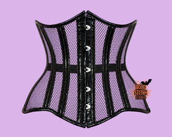 Può includere: Un corsetto nero con un rivestimento in rete viola e pannelli verticali neri lucidi. La chiusura frontale è composta da ganci in metallo color argento. Un piccolo logo con il testo Bold Stitch Studio e un pipistrello è visibile in basso a destra.