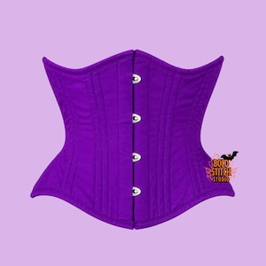 May include: A vibrant purple corset featuring a structured design with vertical paneling and a front closure consisting of four silver-toned metal busk clasps. A small logo with the text Bold Stitch Studio and a bat graphic is visible on the right.