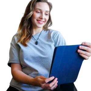 May include: A woman wearing a grey t-shirt and a black pendant necklace holds a blue tablet. The woman is smiling and looking at the tablet. The background is white.