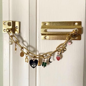 Peut inclure: Une chaîne de porte dorée avec divers charmes, dont un cœur avec un œil, un éclair, un fer à cheval, un trèfle, une lune croissante et une fraise.