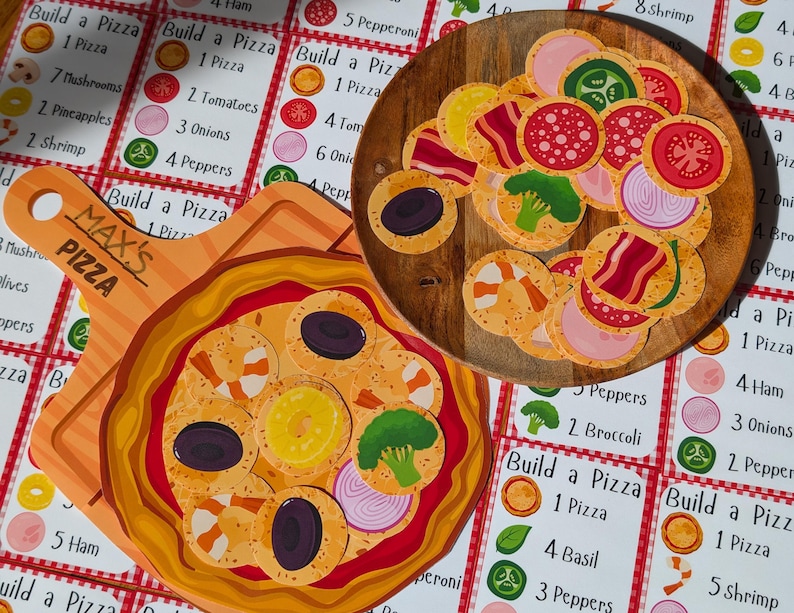 Puede incluir: Un juego para construir pizzas con ingredientes de pizza ilustrados de colores. El juego incluye una tabla de pizza de madera con una variedad de ingredientes, incluyendo pepperoni, champi&ntilde;ones, cebollas, pimientos y camarones. El juego tambi&eacute;n incluye un conjunto de cartas con diferentes recetas de pizza.