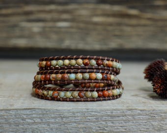 May include: A multi-layered bracelet with brown leather cord and small, colourful, speckled beads. The bracelet is on a wooden surface.